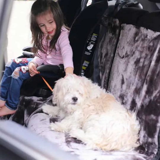 Child sitting with a dog on a car seat cover in a vehicle